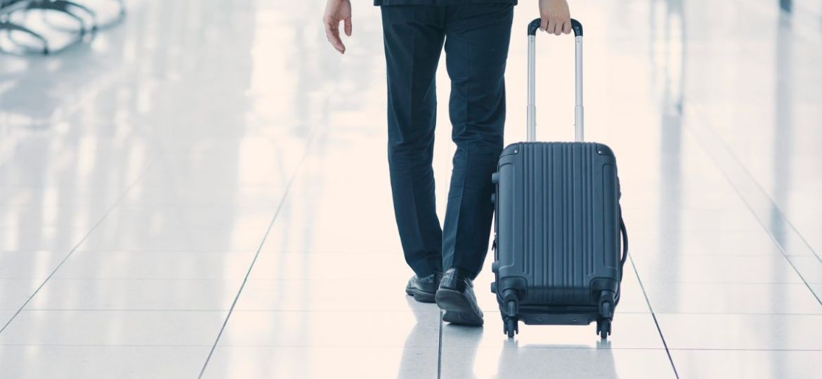 Professional in a dark suit walking through an airport terminal pulling a black rolling suitcase, representing considerations for SSI travel restrictions when planning international or domestic trips.